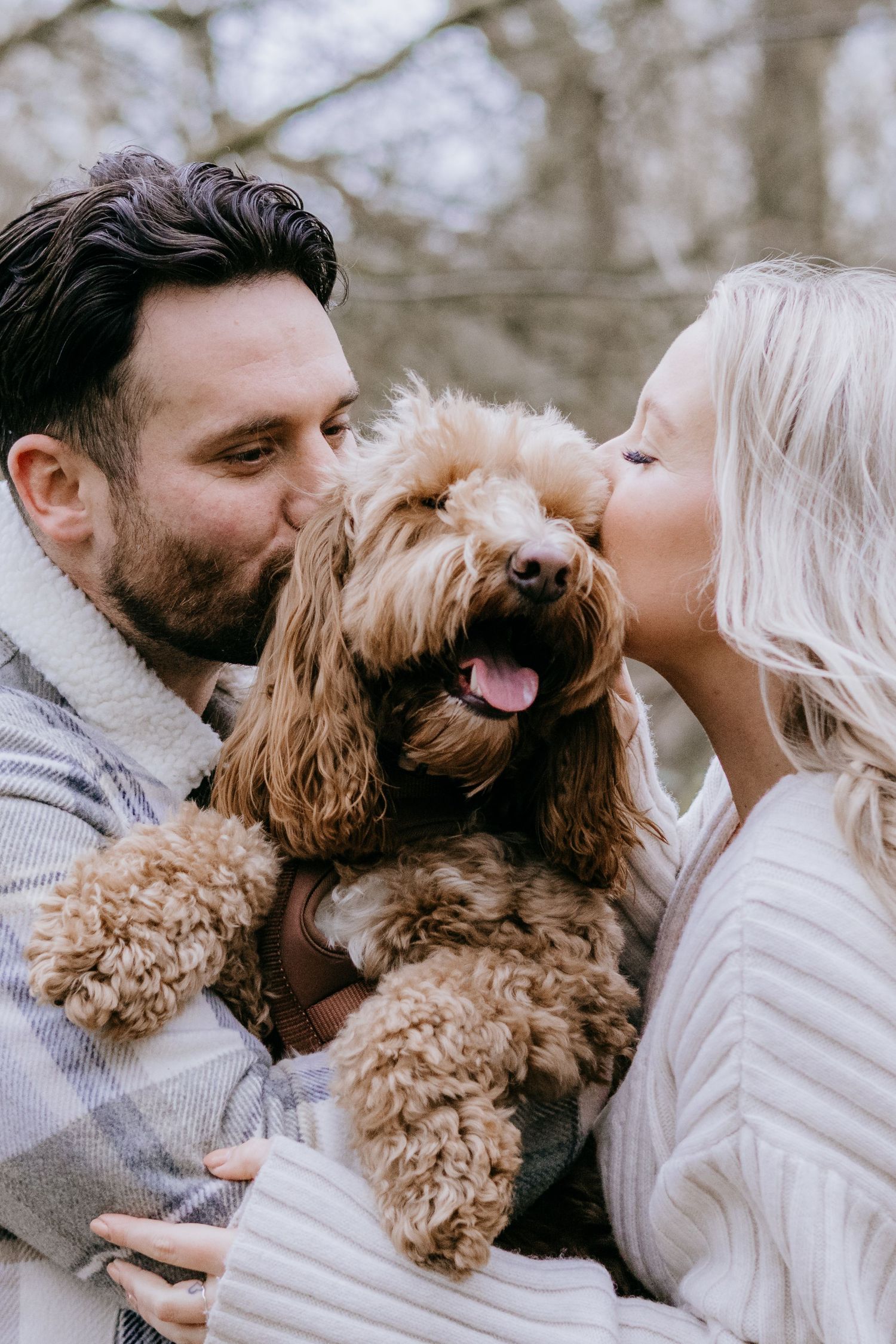 A couple shares affectionate moments with their fluffy golden dog against a winter backdrop.