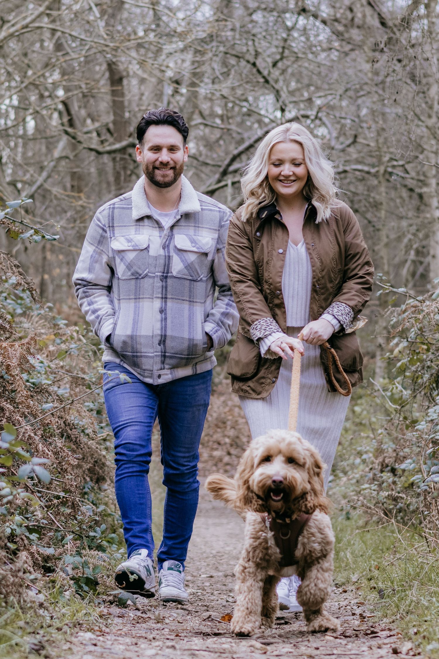 A couple walking their fluffy goldendoodle dog on a wooded trail during autumn.