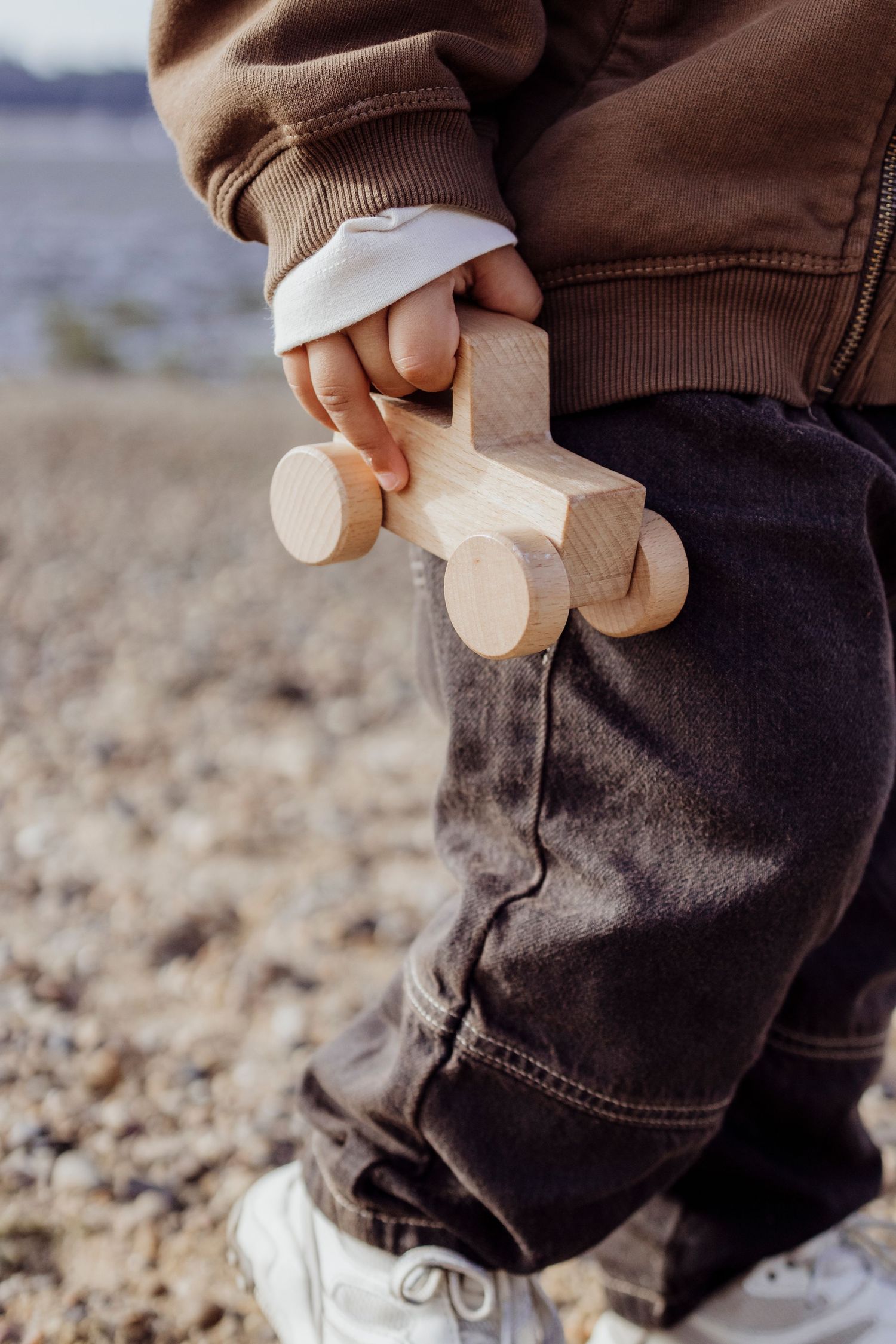 Close-up of small wooden toys being held against dark clothing outdoors.