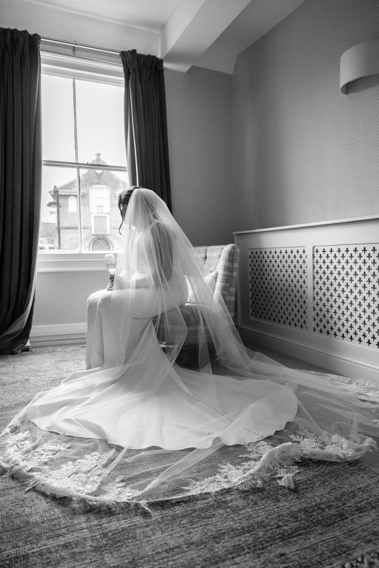 Elegant white wedding dress with flowing train spread across a gray carpeted room in black and white.