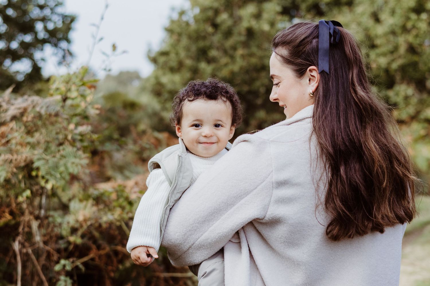 A candid side profile portrait of parent and child sharing a tender moment outdoors.
