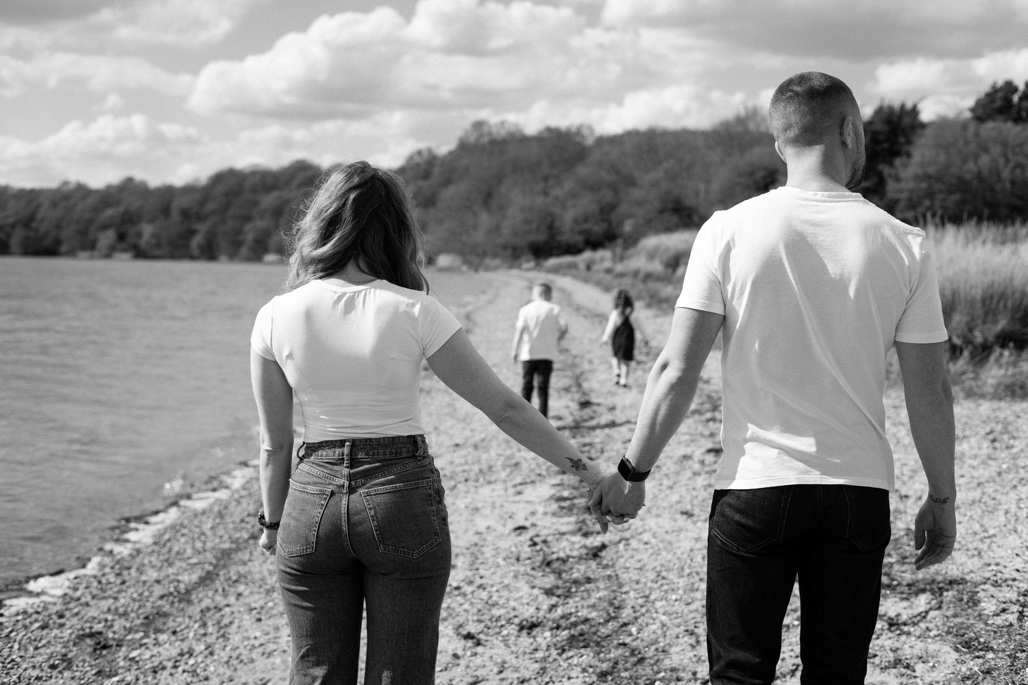 Couple holds hands while walking along a lakeside path with others in the distance.