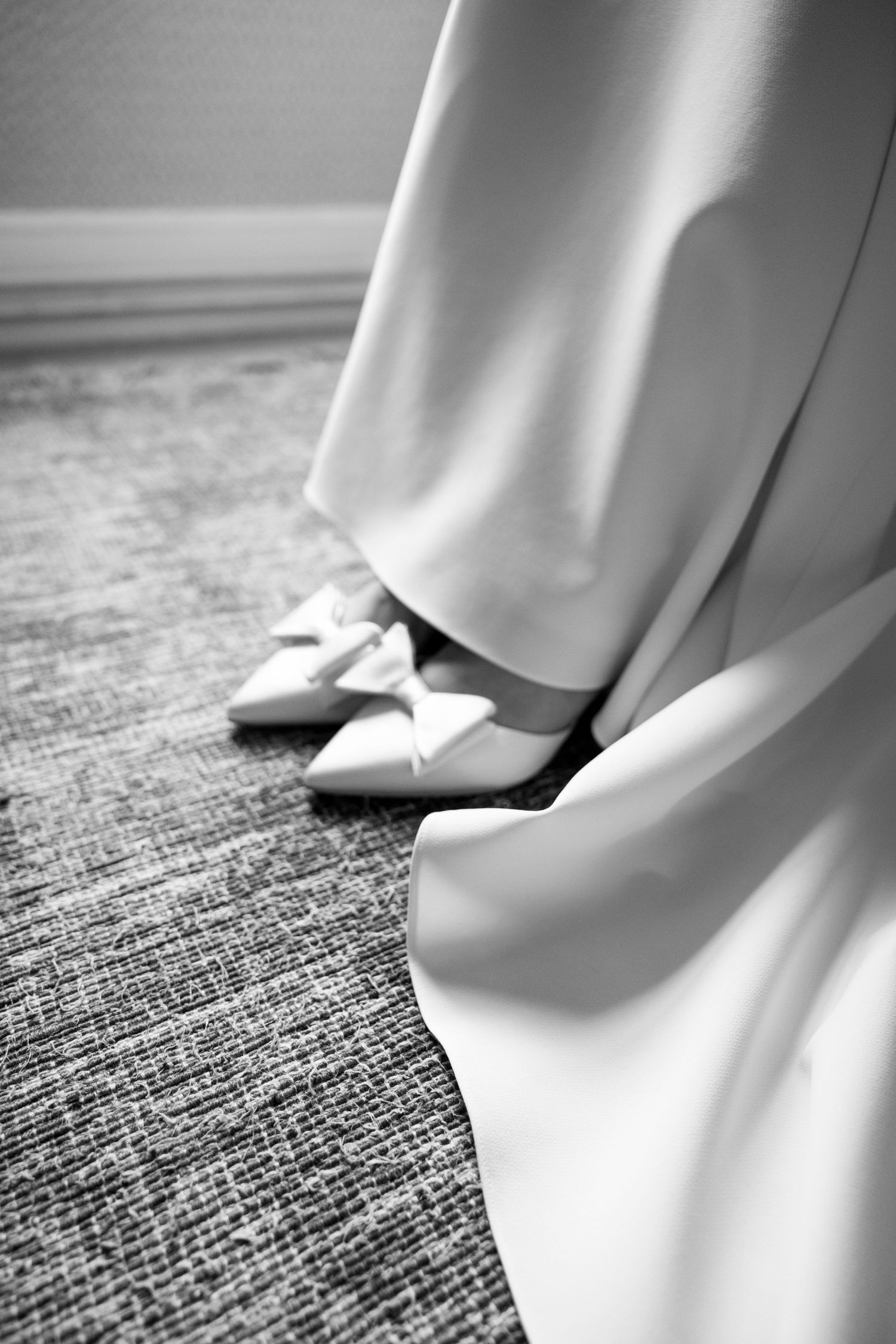 Close-up detail shot of bridal shoes and dress hem on textured carpet.