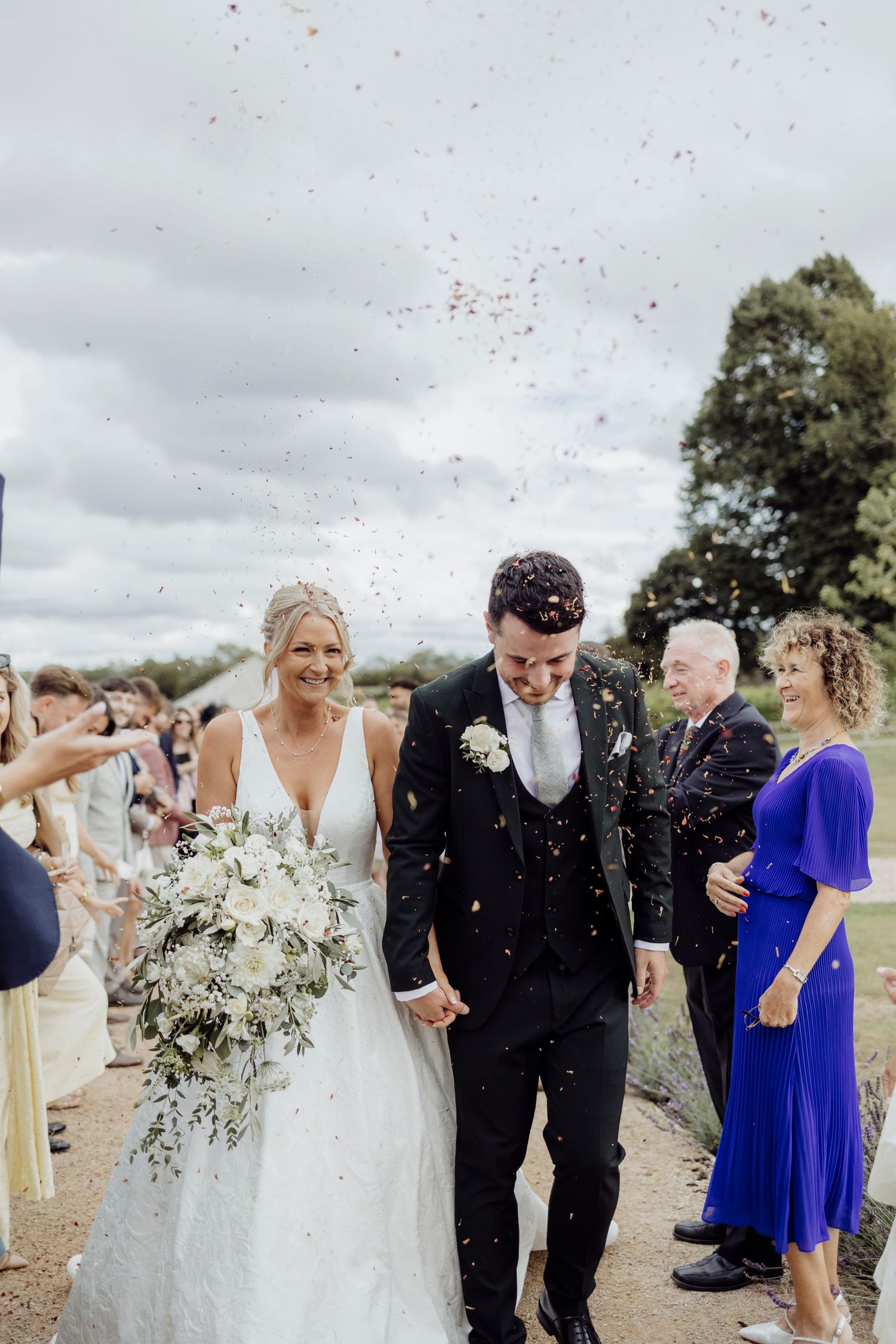 Wedding guests throw confetti over the newlyweds during an outdoor celebration.