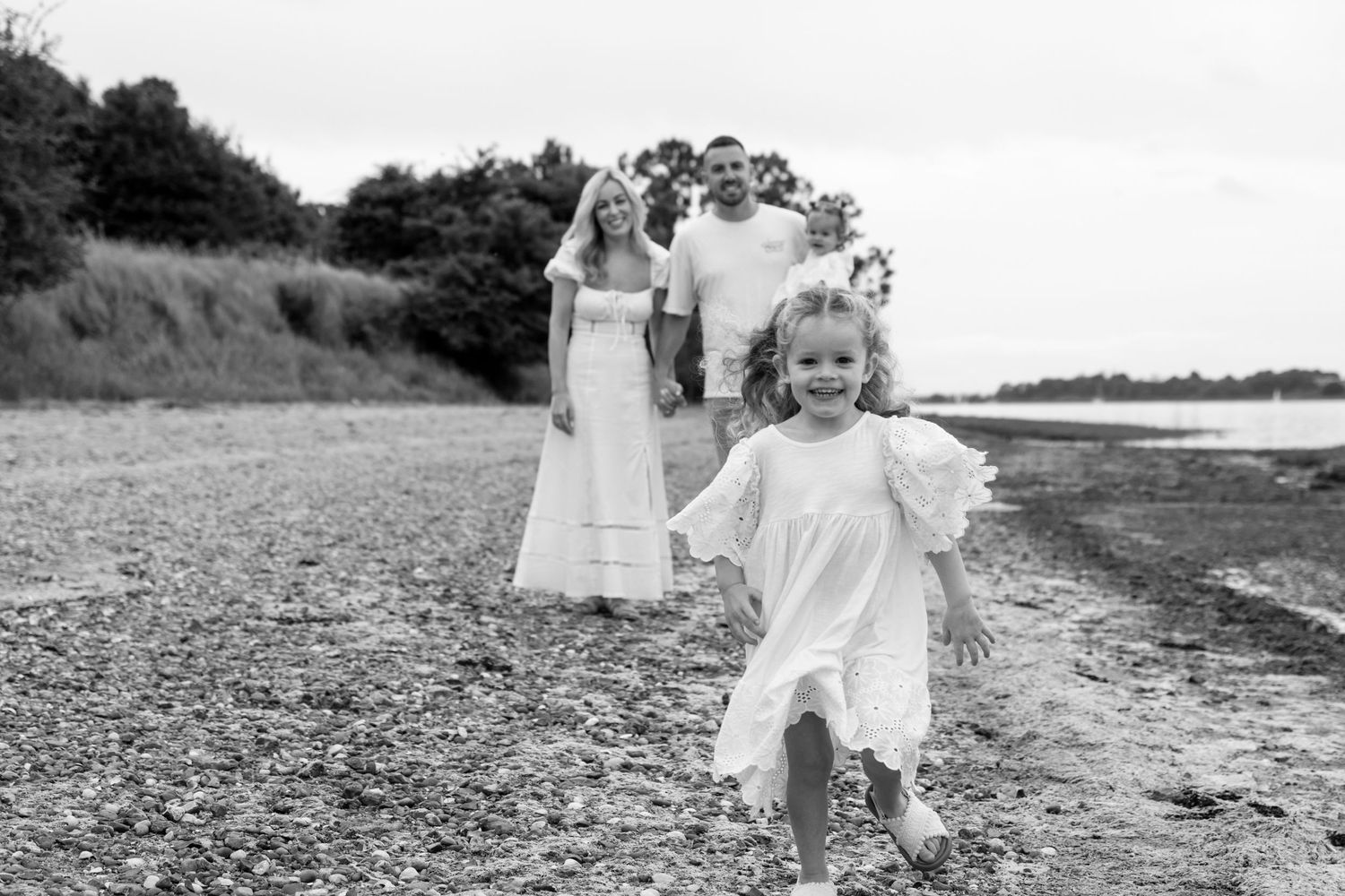 Family strolling along a beach path in white outfits during an overcast day.