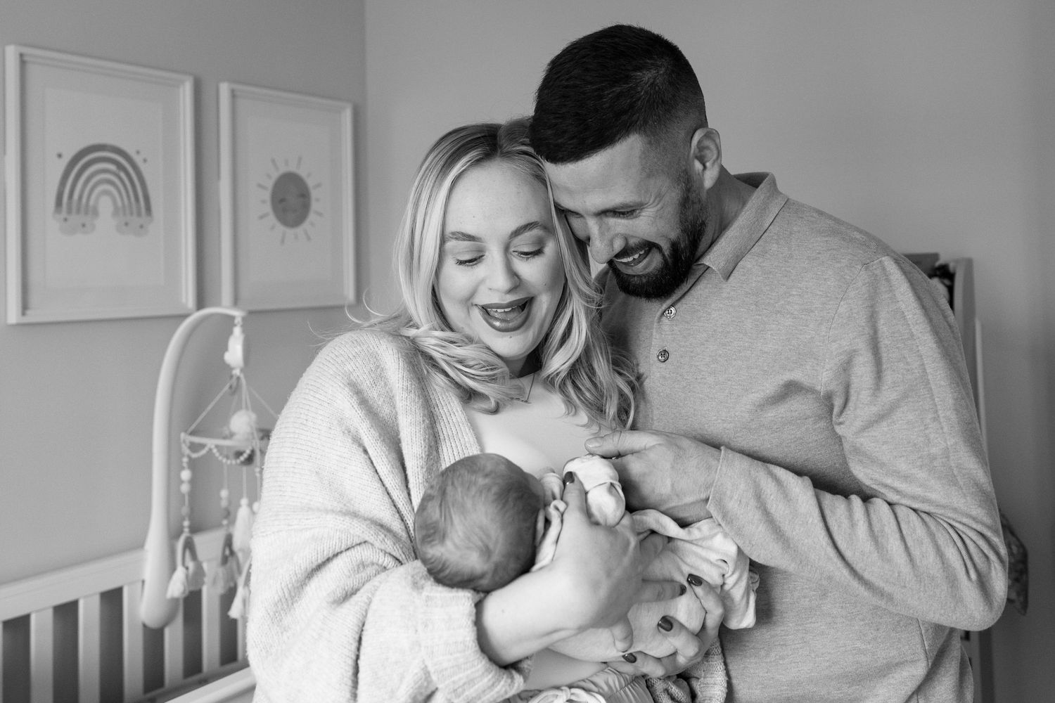 A black and white photo series shows tender moments between a couple and their newborn baby at home.