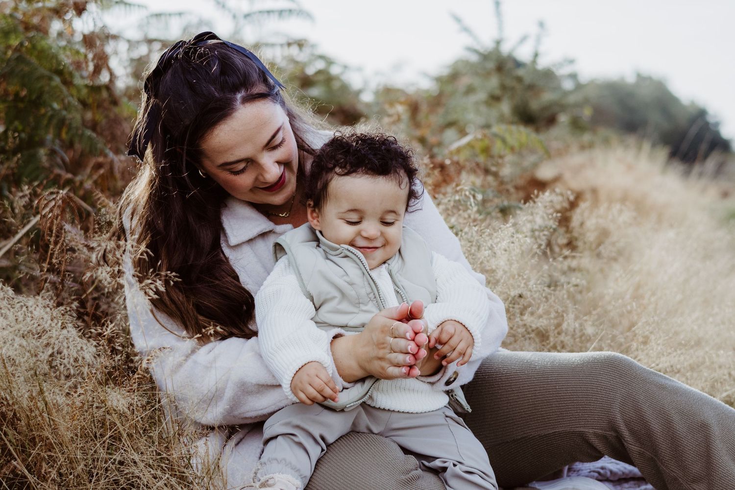 A joyful candid moment between parent and child sitting together in a sunlit autumn field.