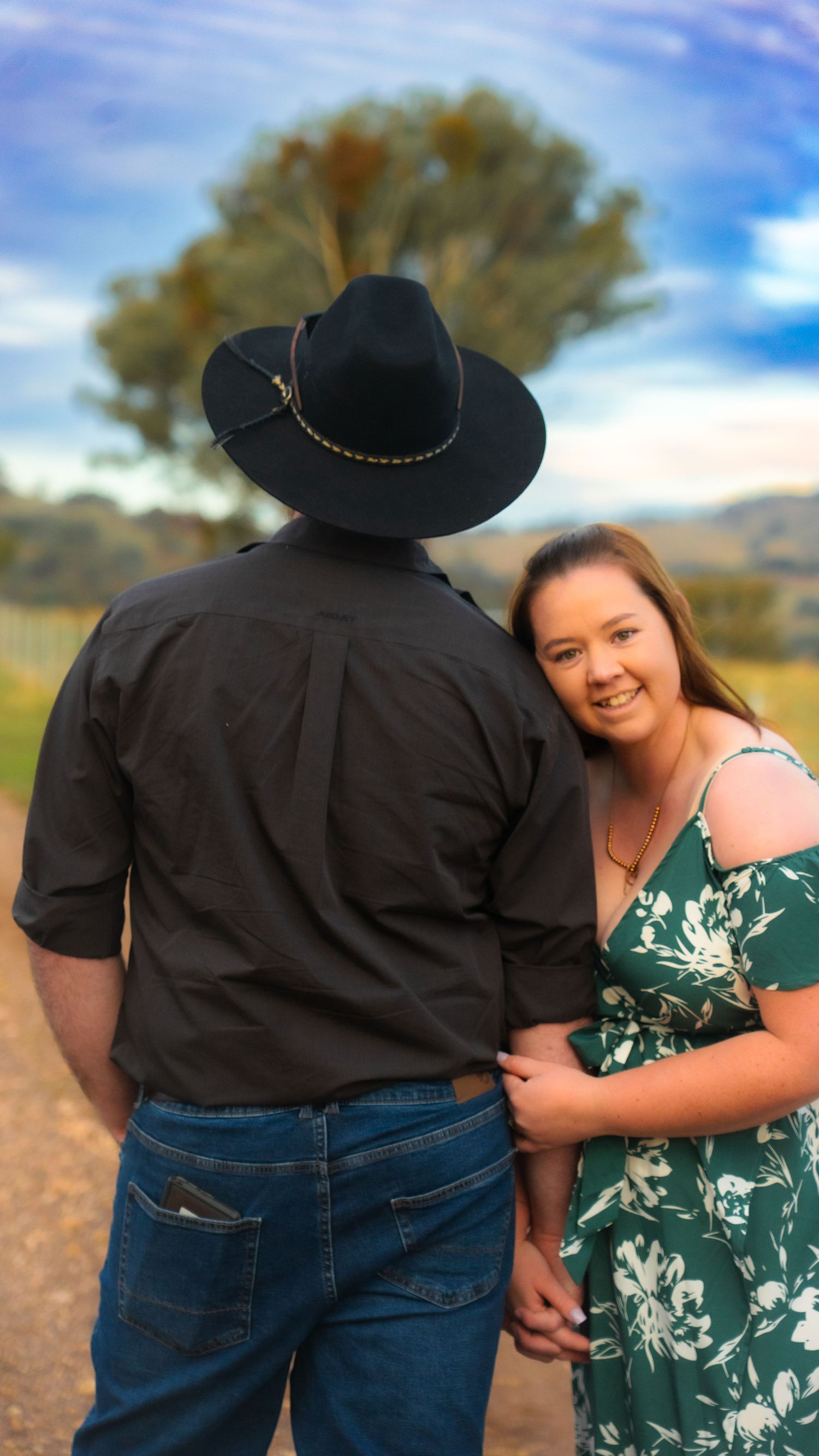 Couple in casual attire sharing a moment outdoors against a cloudy sky.