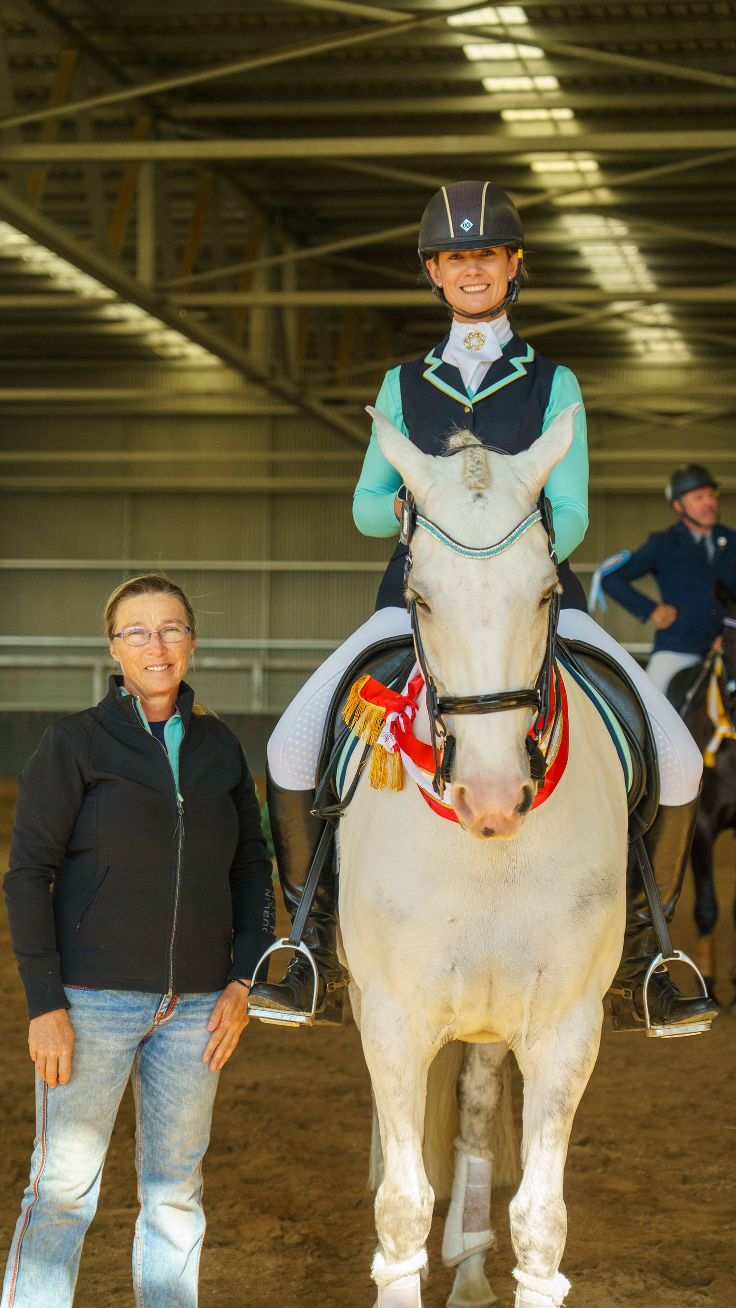 White show horses with handlers in matching outfits performing in indoor arena.