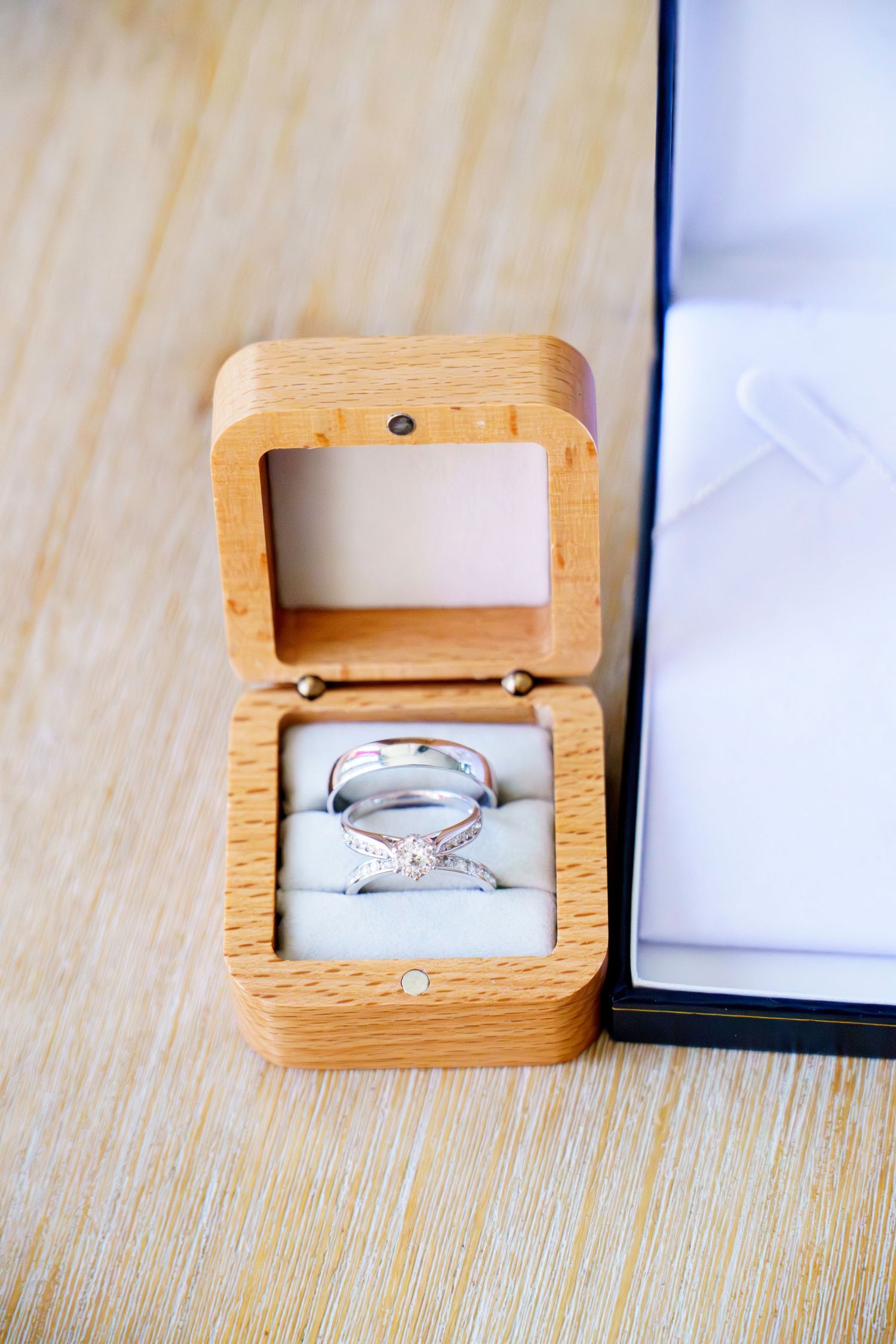 Two silver wedding rings displayed in an open wooden ring box on a wooden surface.
