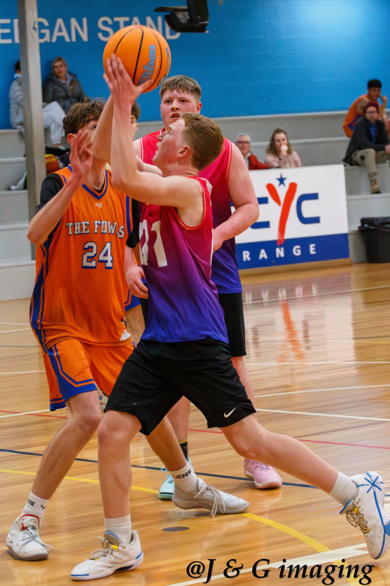 Basketball players in orange and purple jerseys compete during an indoor game.