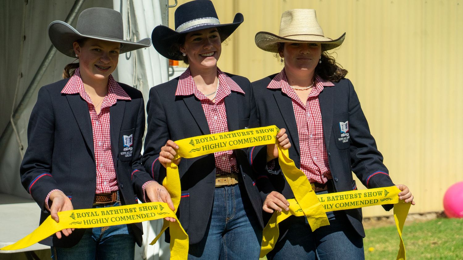 Participants in cowboy hats holding ribbons at an outdoor event.