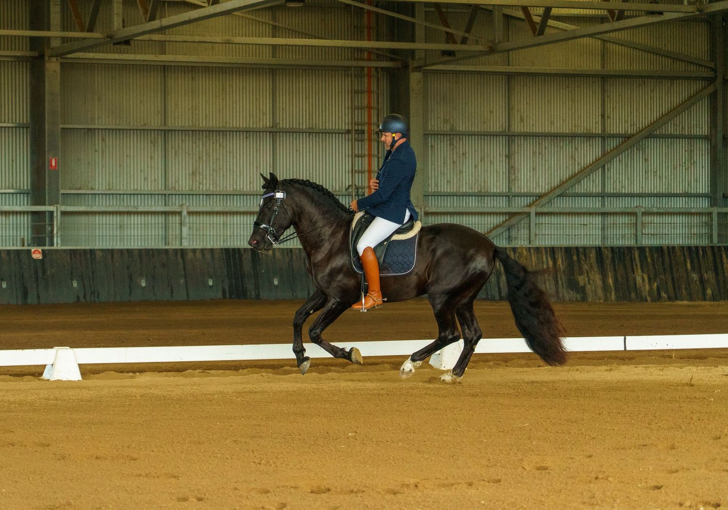 Horses and riders practice dressage movements in a spacious indoor arena.