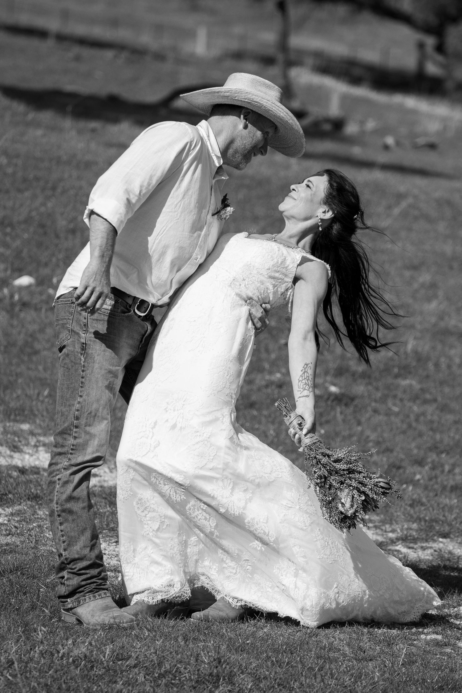 Black and white photo of bride and groom in cowboy hat sharing romantic moment outdoors.
