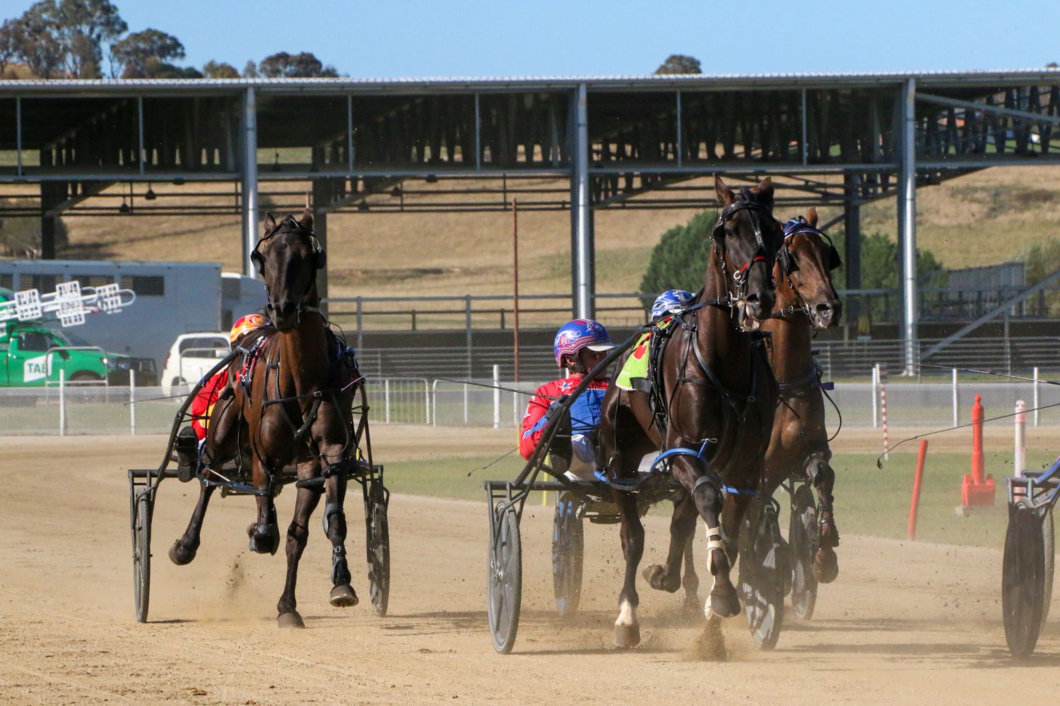 Harness racing horses competing on a dirt track during a race event.