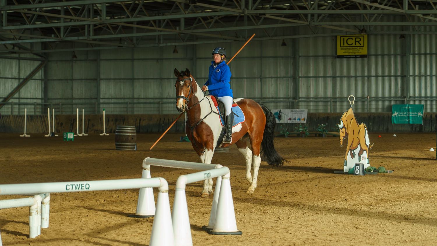 Multiple horses and riders compete in a show jumping event at an indoor arena.