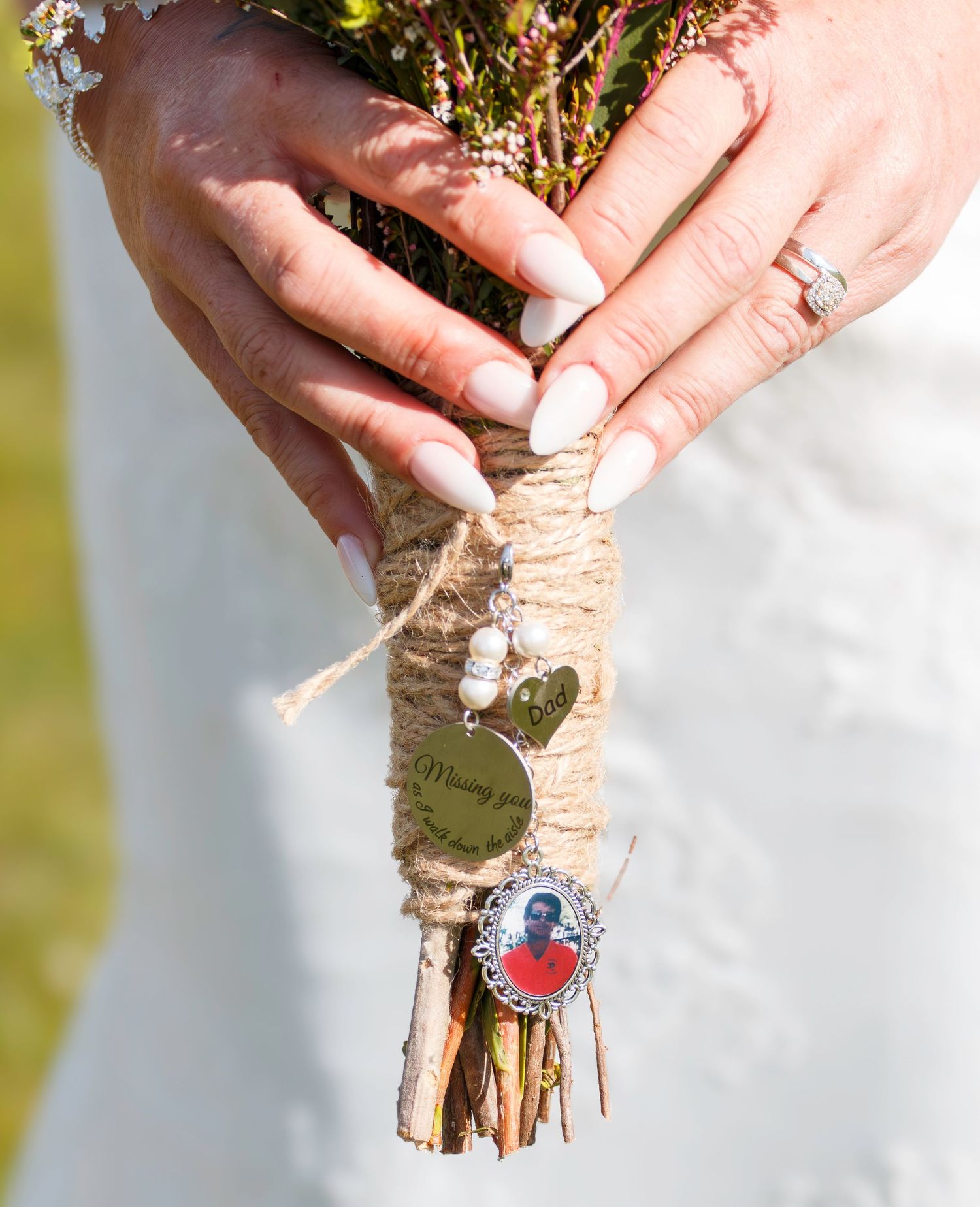 Bride holding rustic wedding bouquet wrapped in twine with pearl charms and a memorial photo pendant.