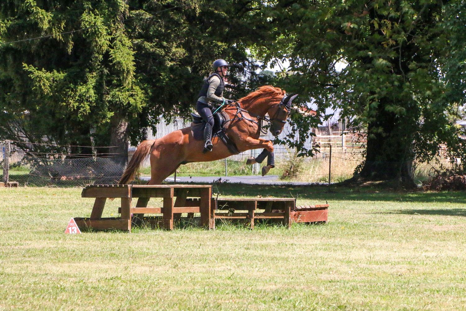 Horses leap over cross-country jumps on a grassy course.