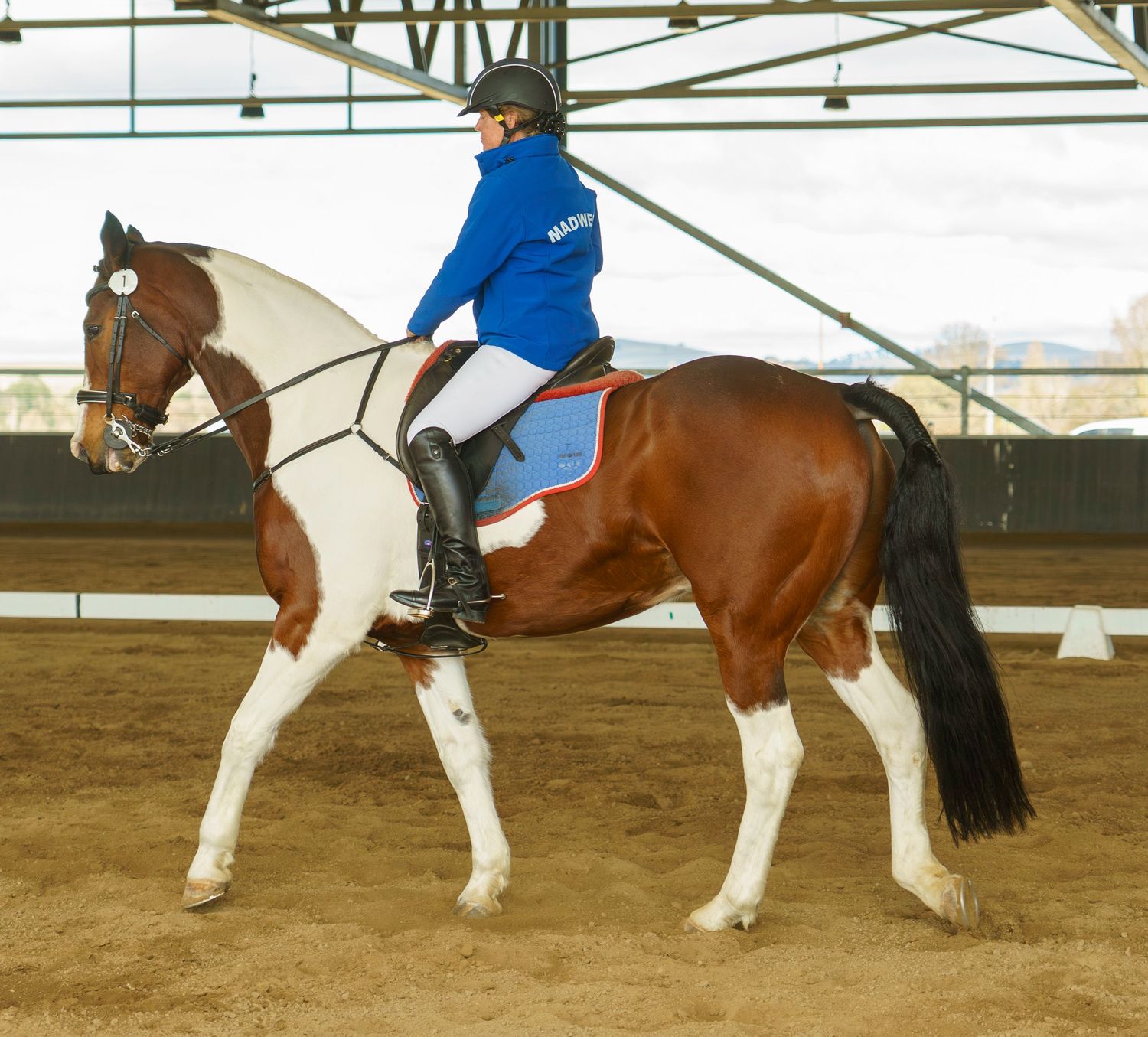 Riders practice horseback riding techniques in formation at an indoor equestrian center.