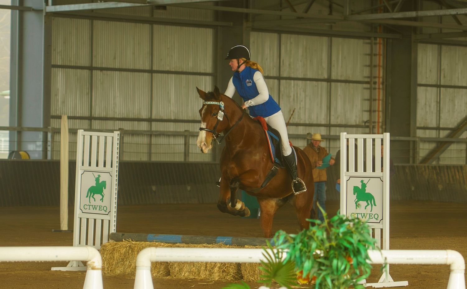 Equestrians practice riding patterns between markers in a covered arena.