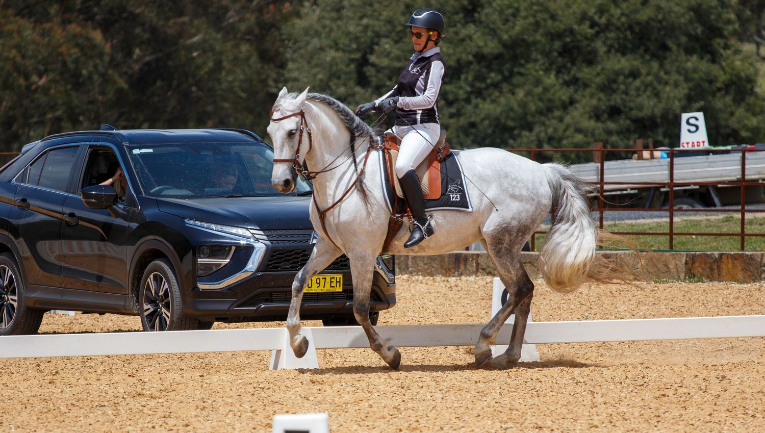 Equestrians perform dressage routines in a sandy outdoor arena.