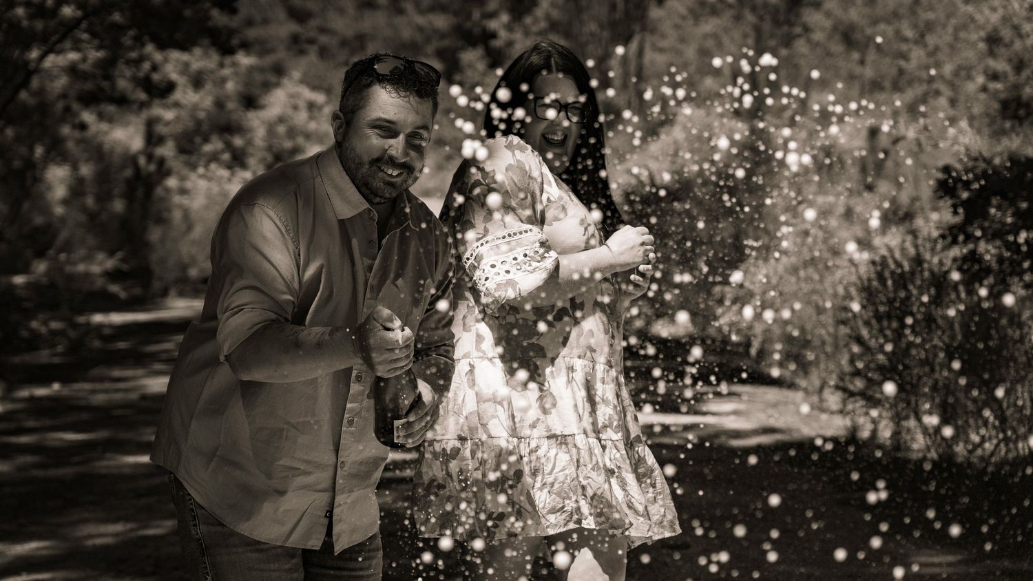 Black and white photo of a couple holding a baby outdoors, surrounded by sparkling bokeh lights in a garden setting.