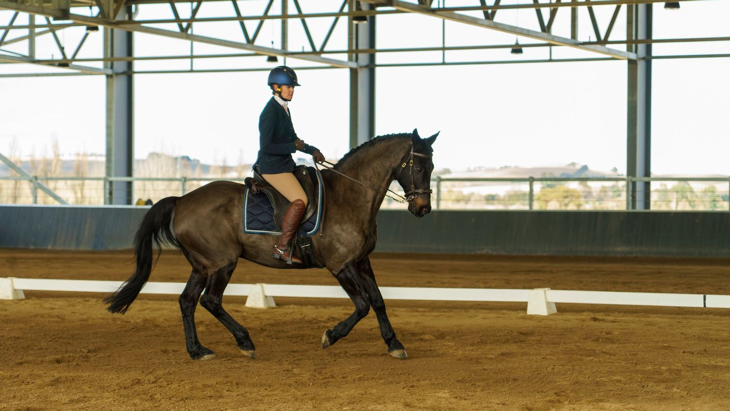 Riders guide their horses through training exercises in a well-lit indoor arena.
