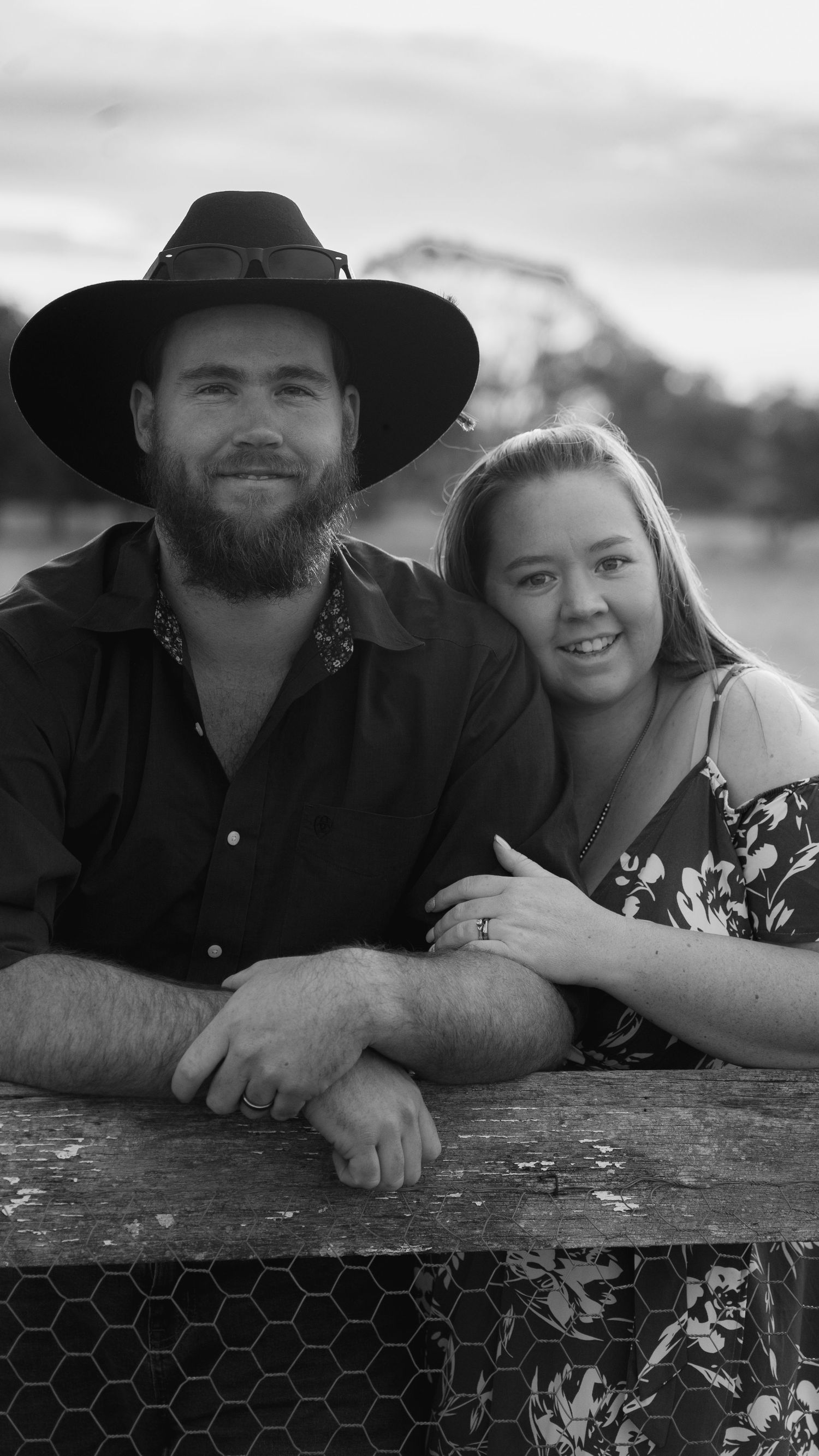 Black and white portrait of couple leaning on wooden fence in countryside.