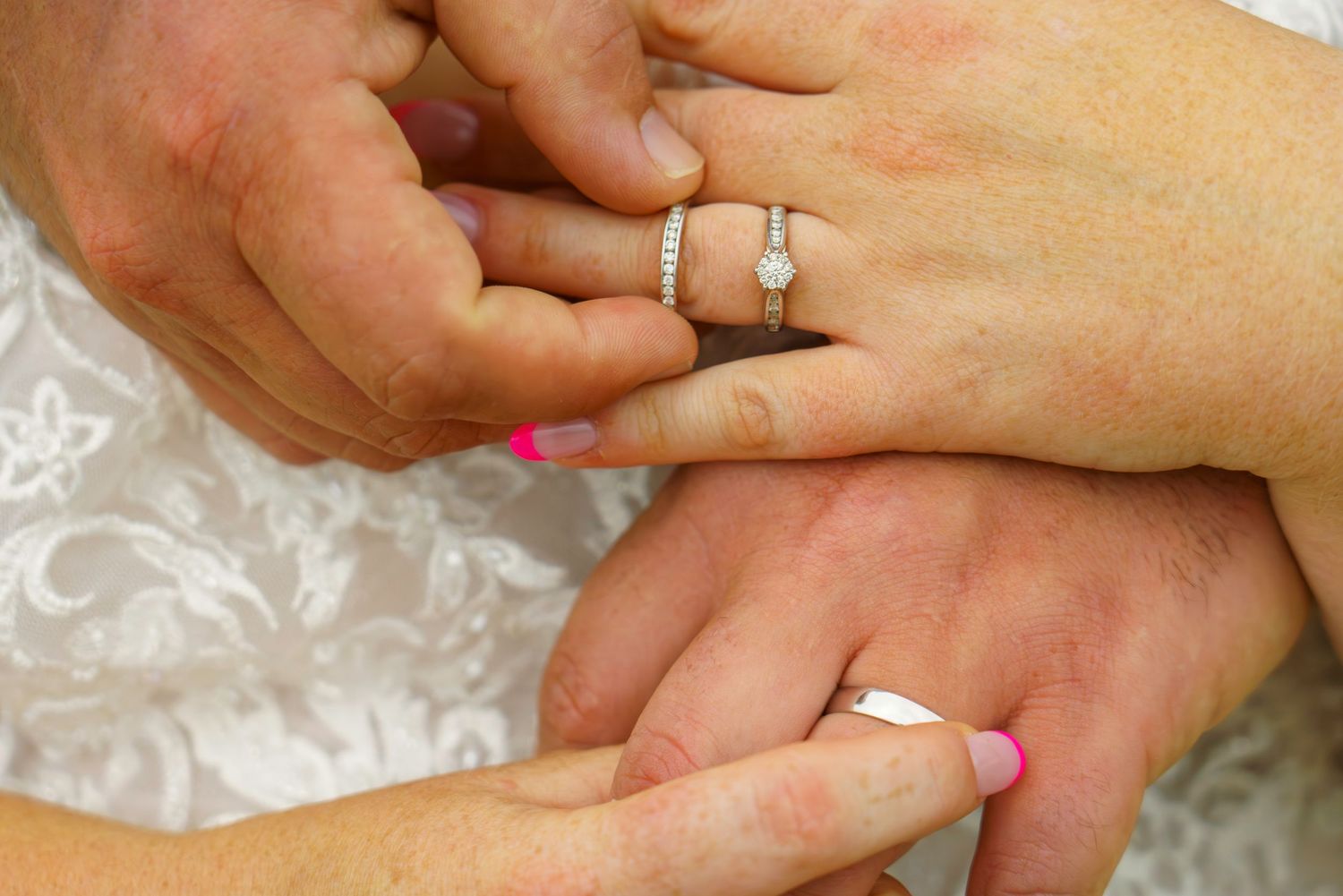 Close-up of wedding ring exchange, bride wearing diamond engagement ring with pink manicure.