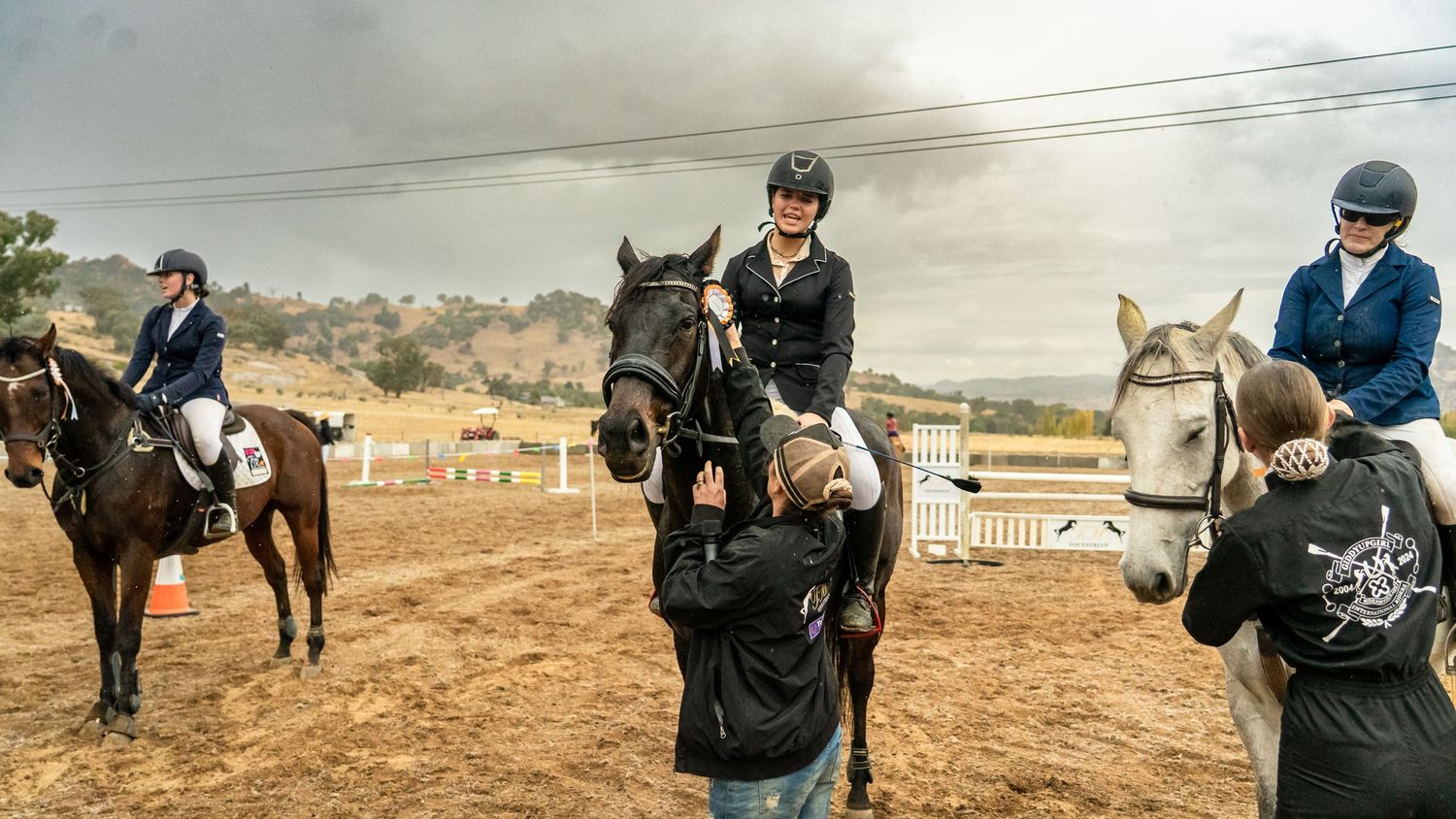 Horse jumping competition on a dusty field with multiple riders.