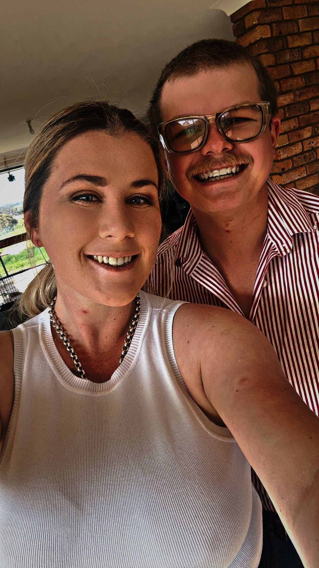 Two people taking a close-up selfie together against a brick wall background.