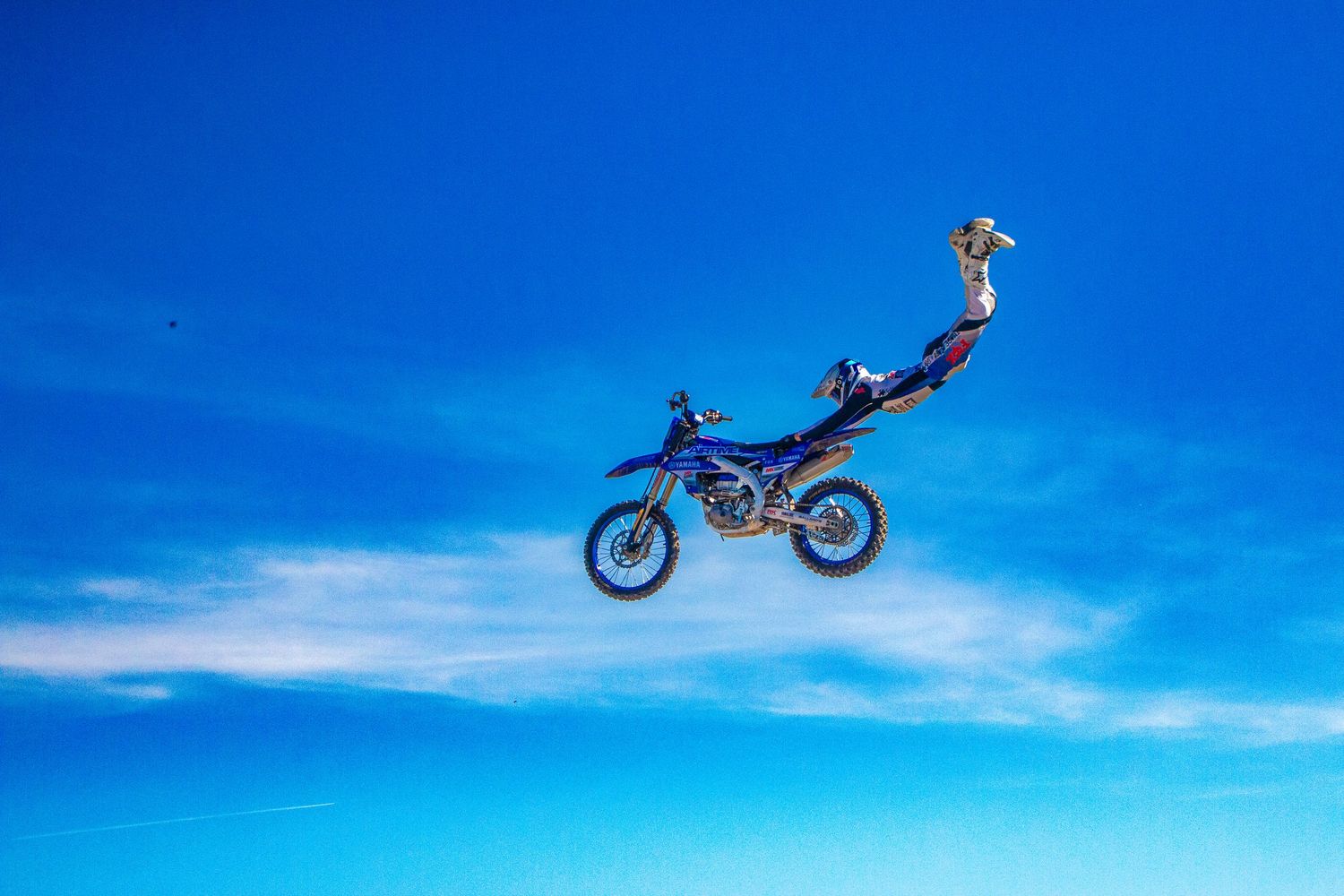 Silhouette of motocross bike performing jump against bright blue sky.