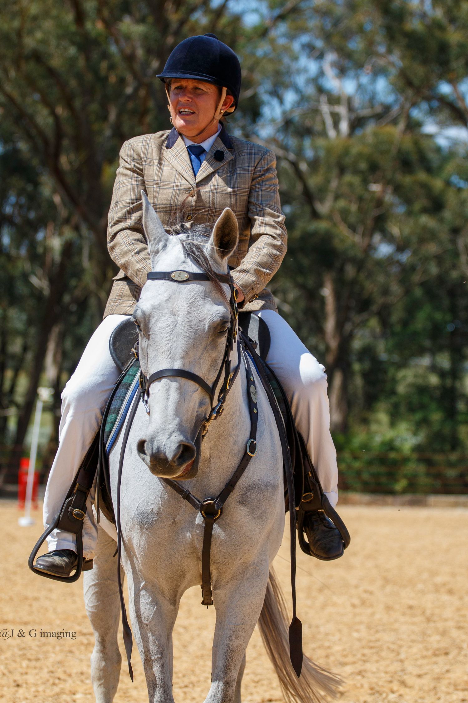 Equestrian rider in formal attire aboard a white horse during competition.