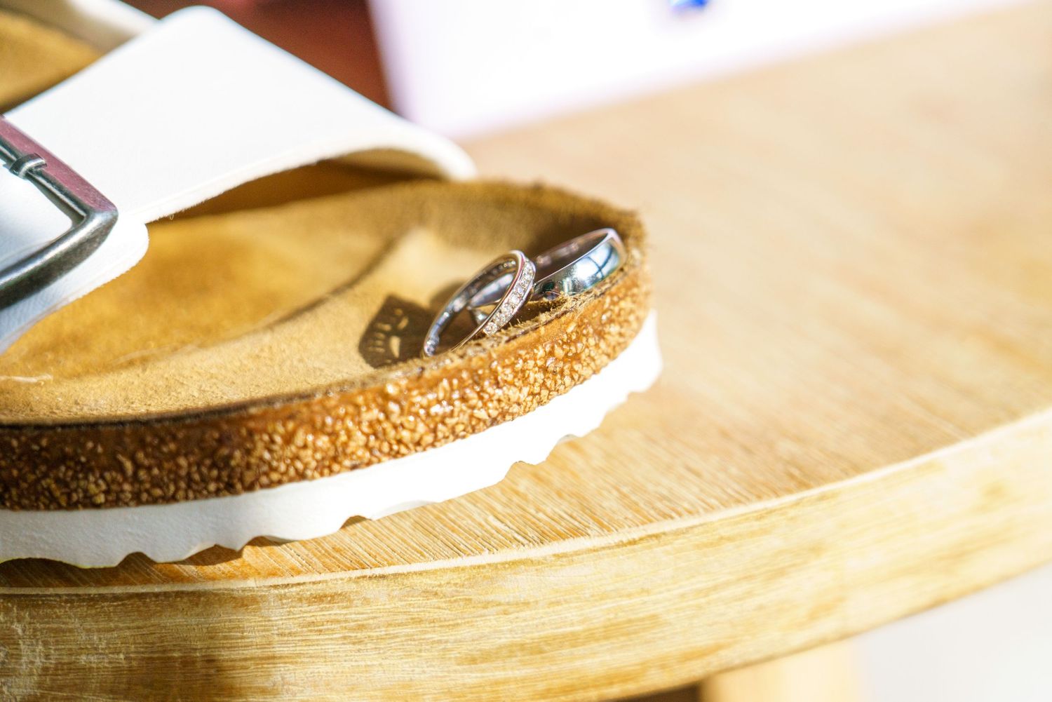 Close-up of a tan suede Birkenstock sandal with cork sole and metal buckles resting on a wooden surface.
