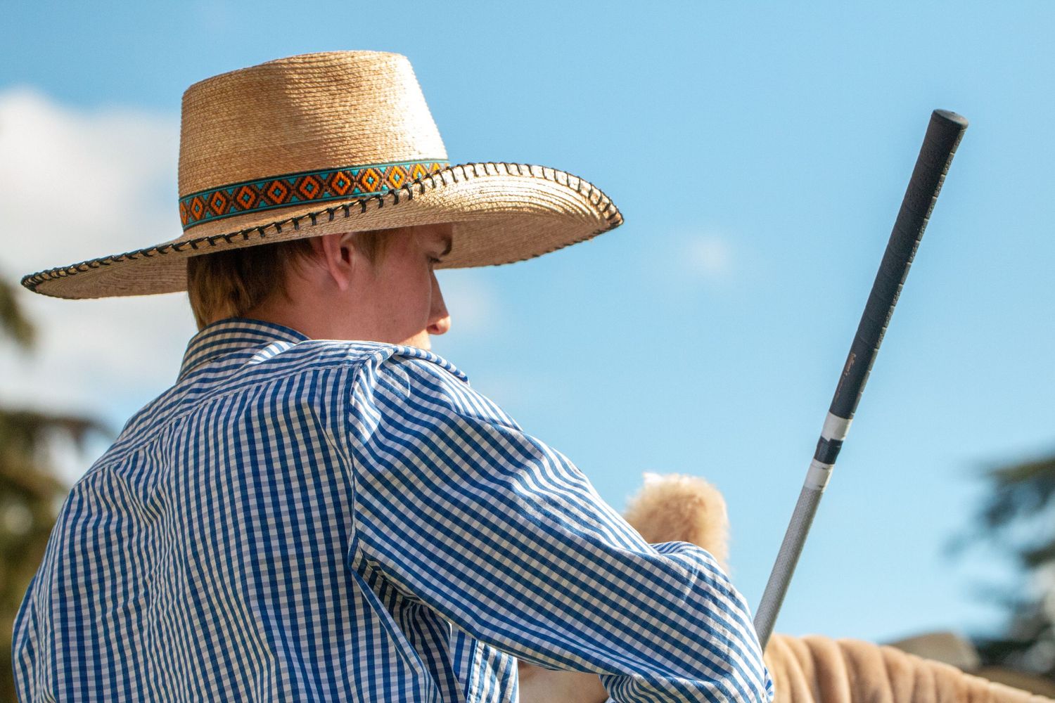 Competitors in western attire and straw hats at an outdoor equestrian event.