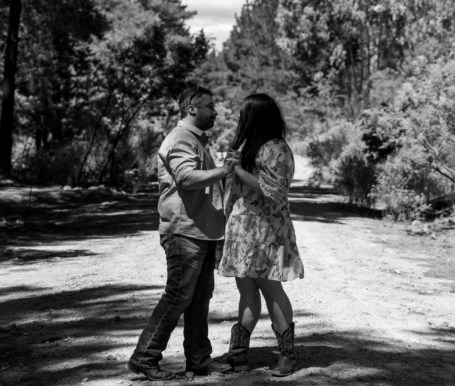 Black and white photo of a couple dancing together on a dirt path surrounded by trees in a natural outdoor setting.