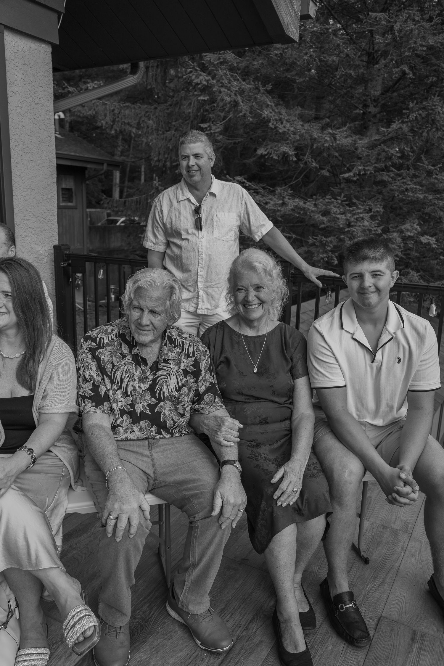 Black and white family portrait of five people posing on a deck outdoors, with trees visible in the background.