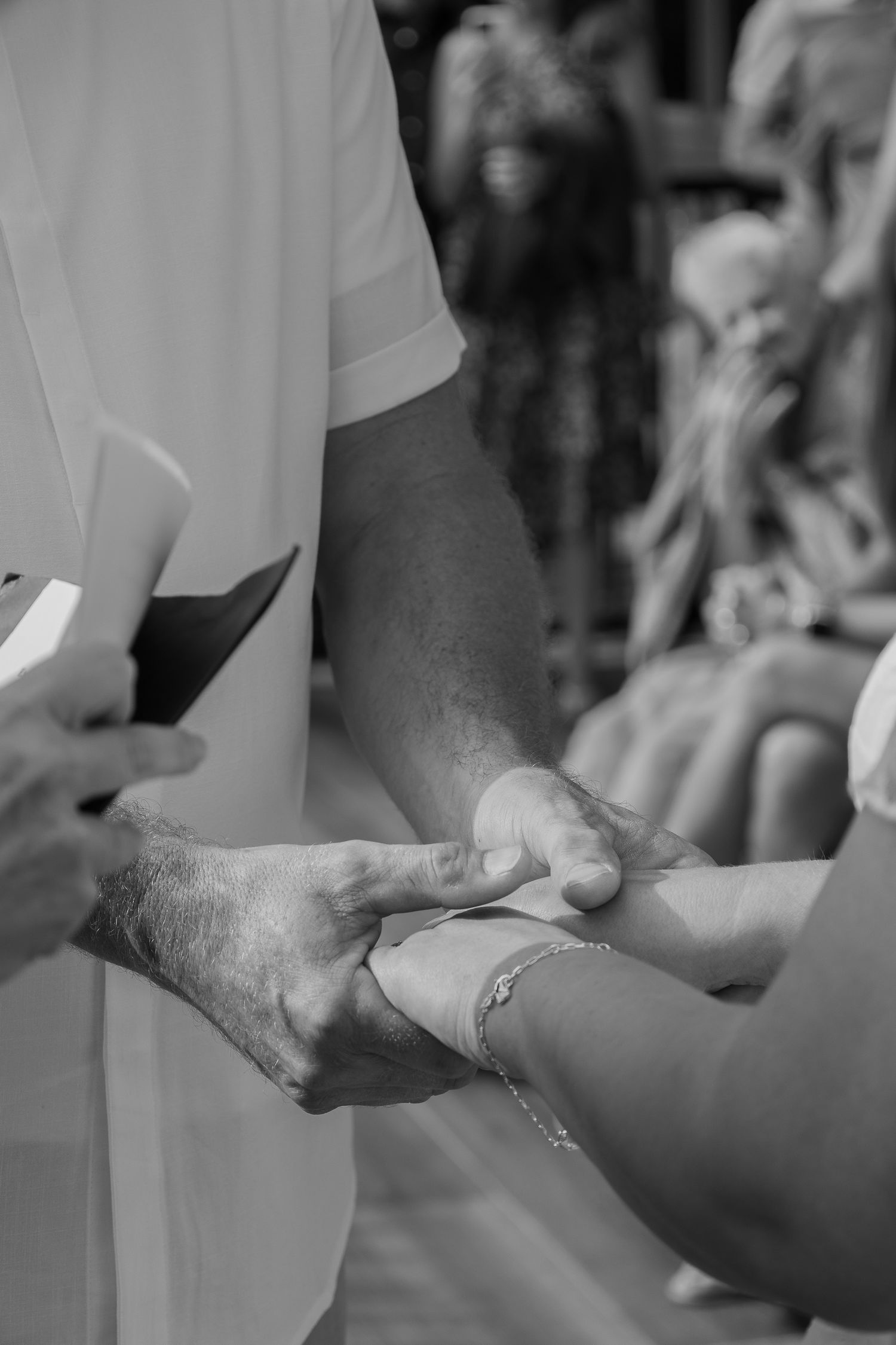 Black and white photo of elderly hands holding a younger persons wrist during a wedding ceremony.