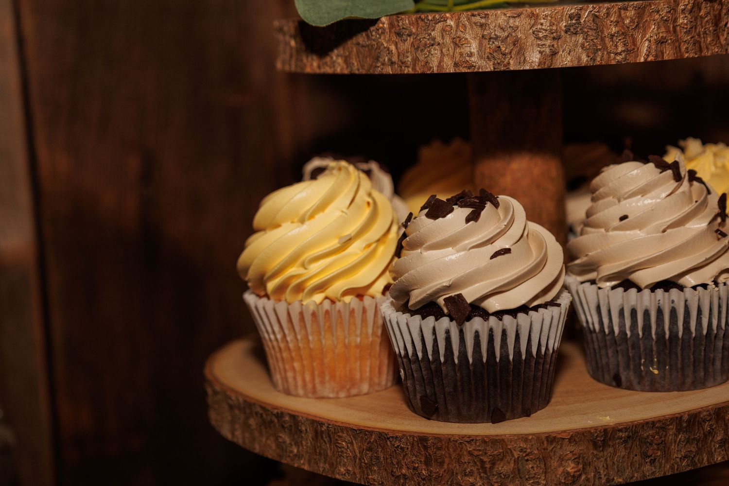 Assorted gourmet cupcakes with swirled frosting displayed on a rustic wooden tiered stand.