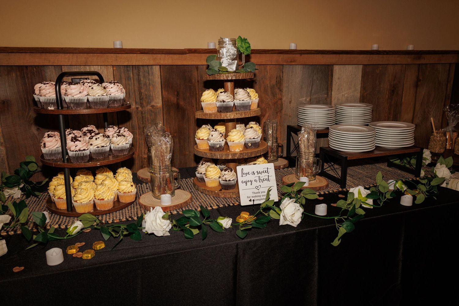Wedding dessert table featuring tiered cupcake display with white roses and assorted treats.