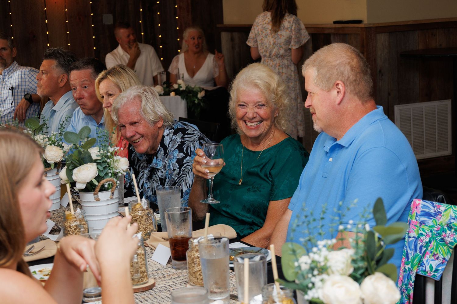 Guests laughing and celebrating at a wedding reception dinner, dressed in elegant attire at a decorated table.