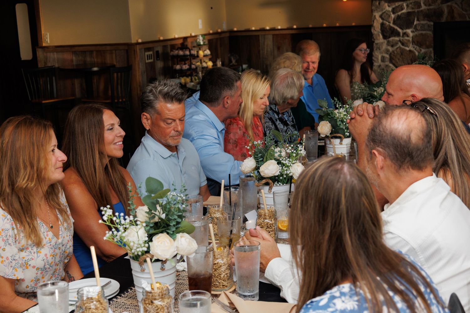 Guests laughing and socializing at a festive indoor dinner party with floral centerpieces on a long table.