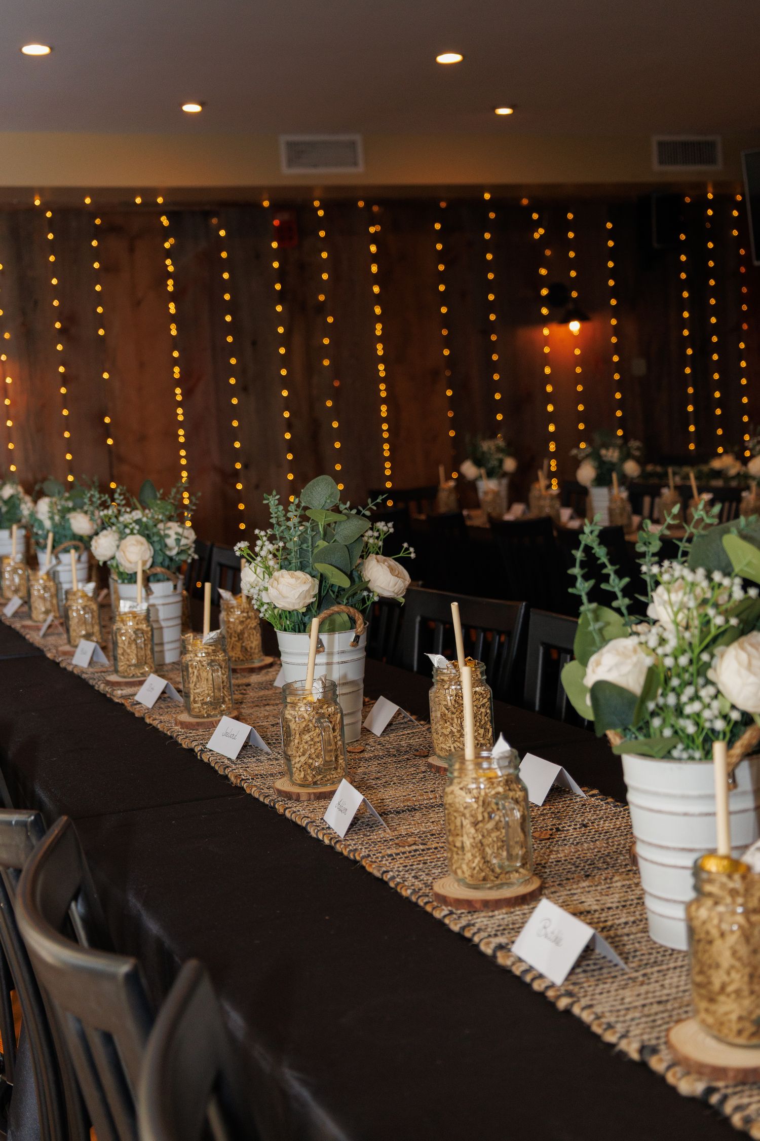 Elegant wedding reception table with white floral centerpieces, mason jars, and warm string lights.