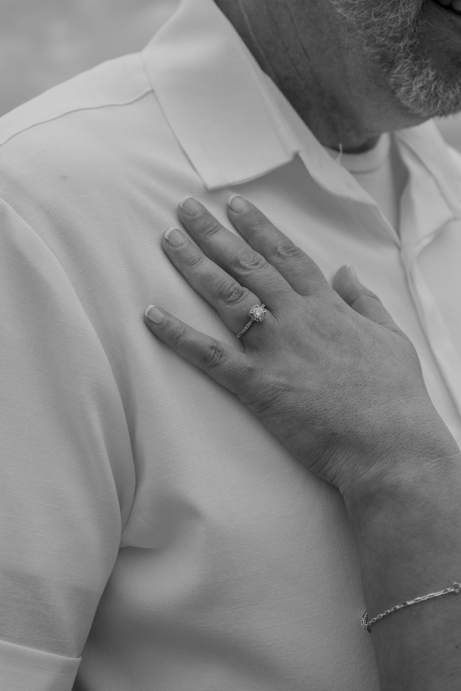 Close-up black and white photo of brides hand with engagement ring resting on grooms white shirt.