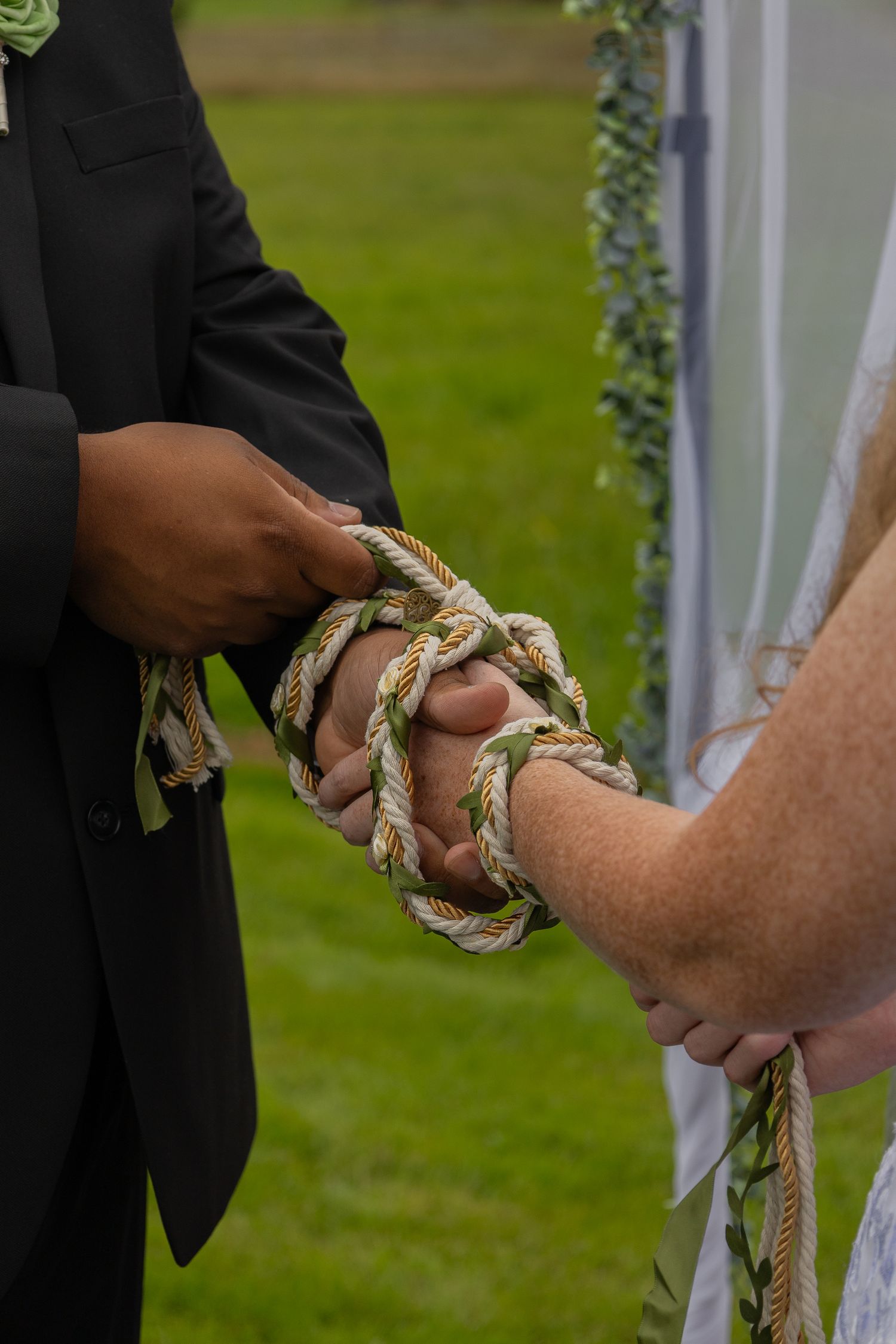 Hands bound together with decorative rope during a handfasting wedding ceremony outdoors.