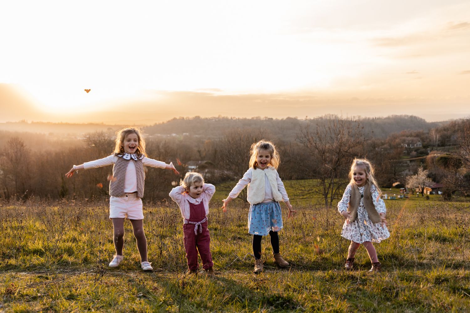Séance photo famille en Isère : quatre jeunes filles s'amusant dans une prairie au coucher du soleil.