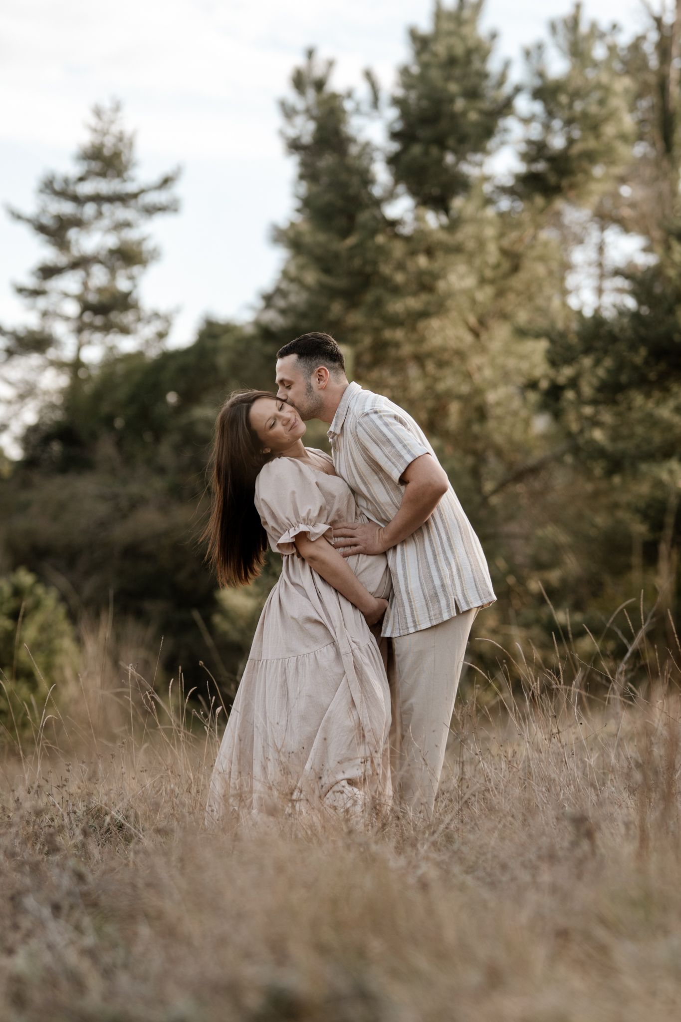 Séance photo couple en Isère : un baiser romantique et complice au cœur d'une clairière en forêt pour célébrer l'arrivée de bébé.