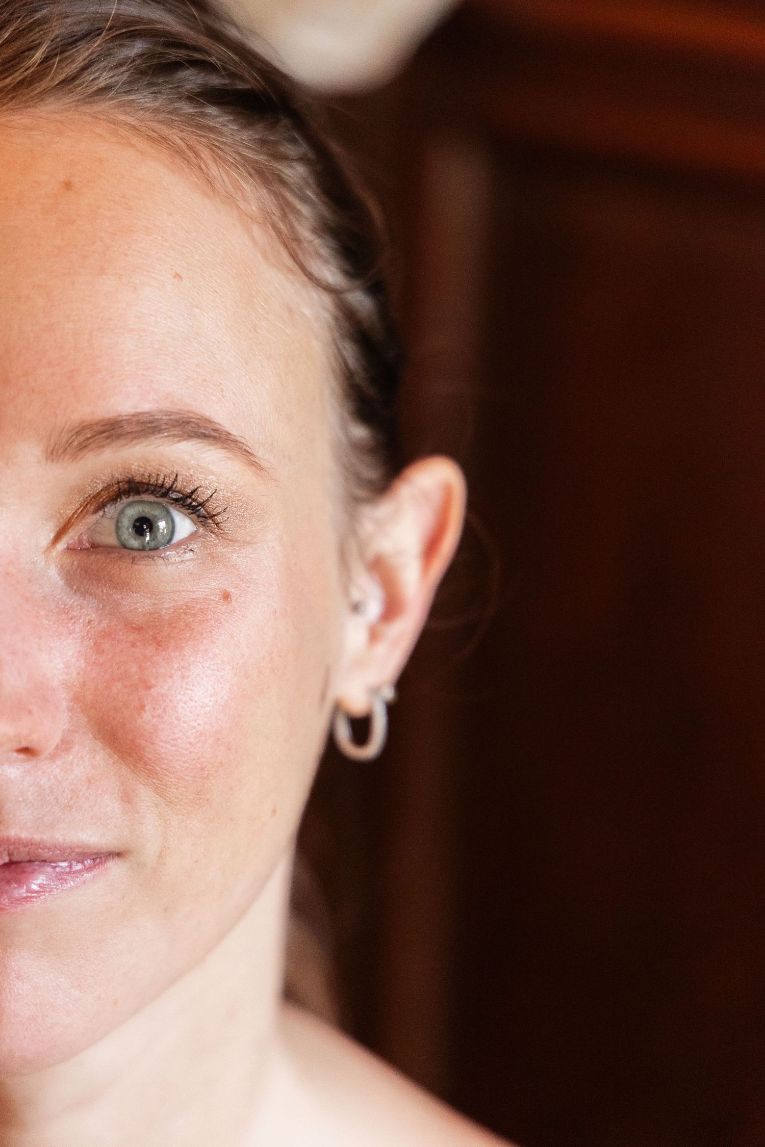 Close-up half portrait of bride with green eyes, freckles, and silver hoop earrings on wedding day.