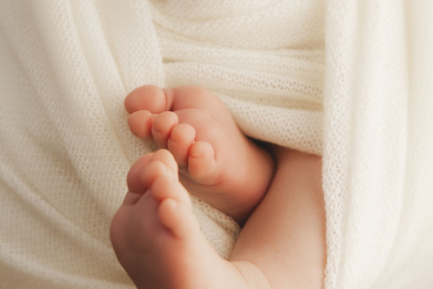 Close-up of tiny newborn baby feet peeking out from a soft white knit blanket.