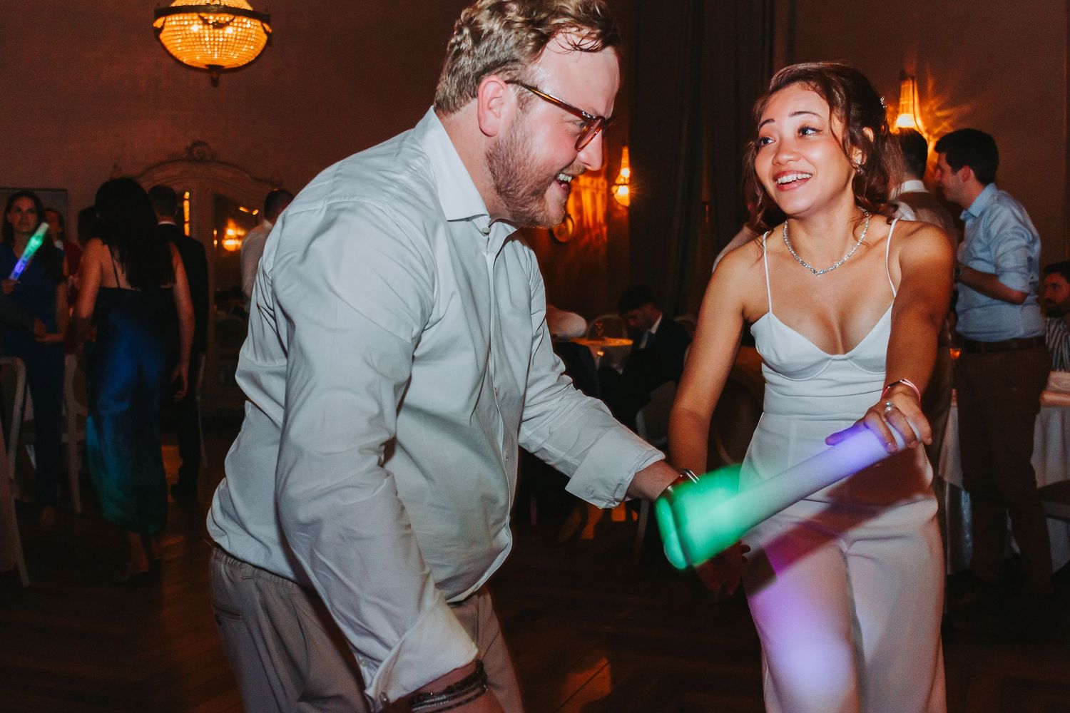 Couple dancing together at a wedding reception holding glowing light sticks on the dance floor.